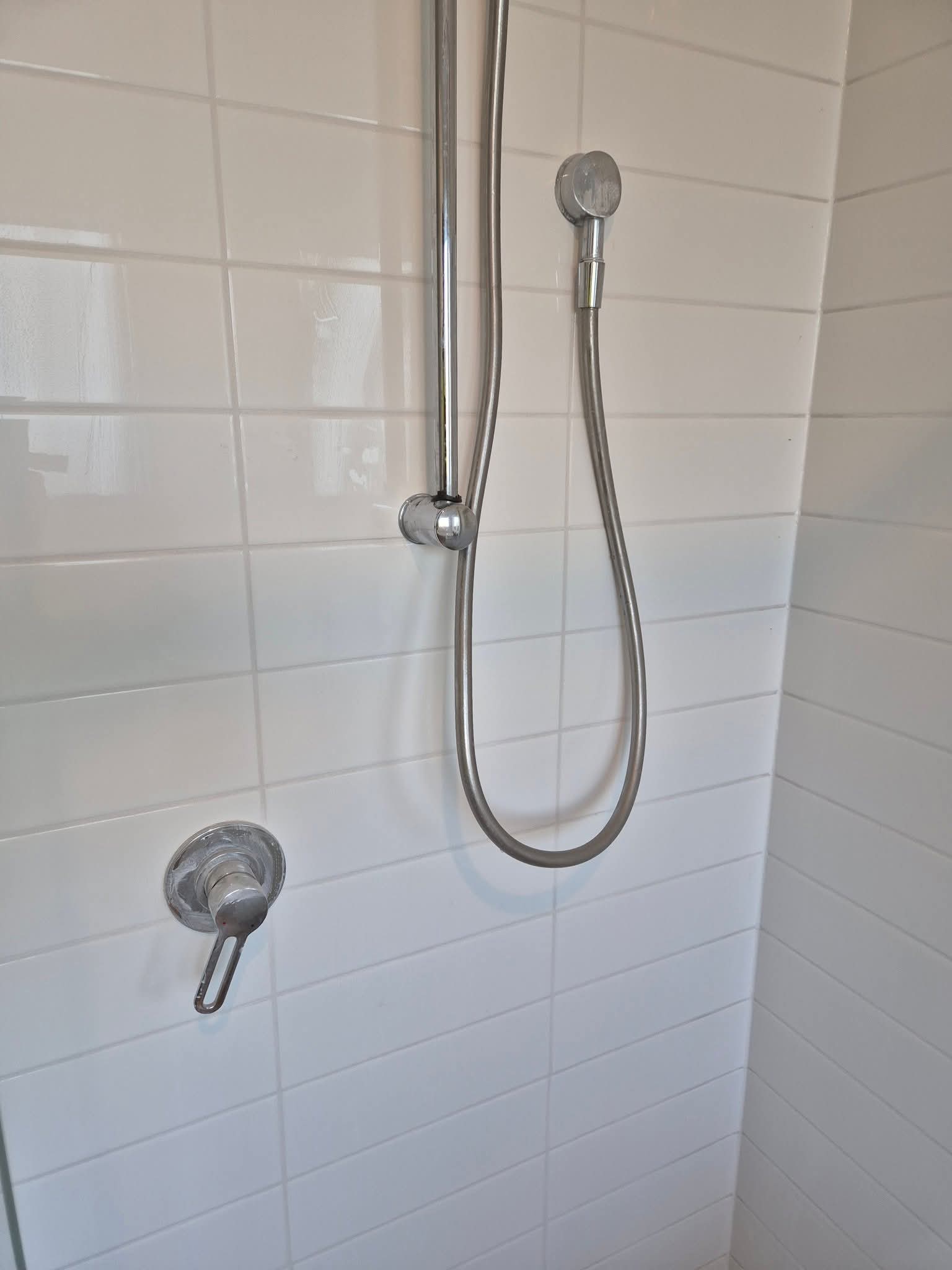 Restored white-tiled shower with chrome handheld fixture.