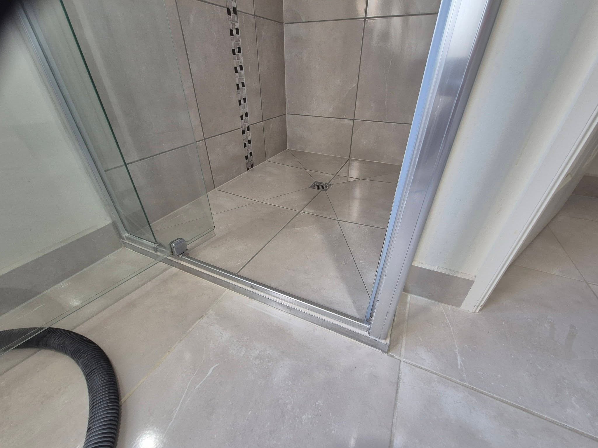 Close-up of a tiled shower floor with glass door and a drain in the center.