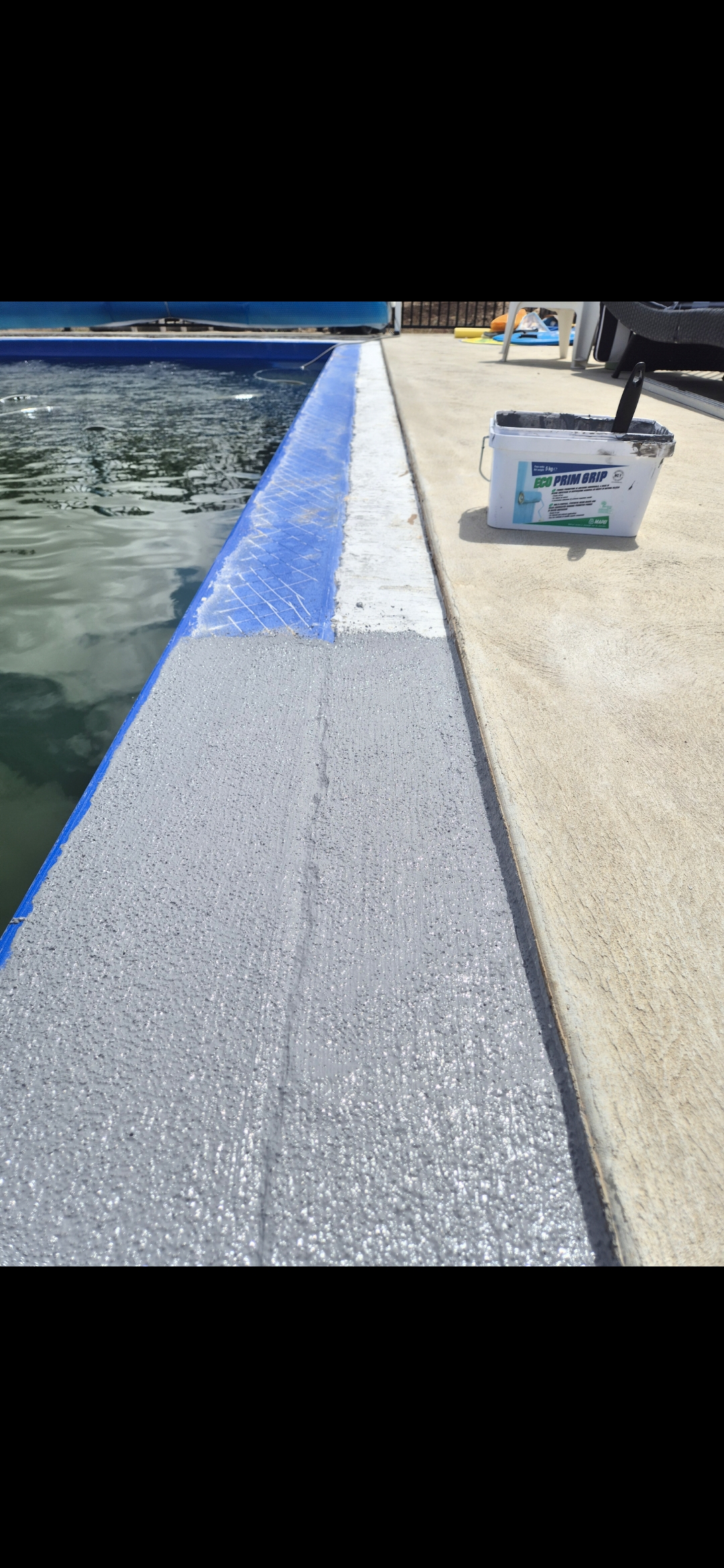 Paint bucket labeled ECO PRIM GRIP next to a swimming pool edge, partially painted with gray primer.