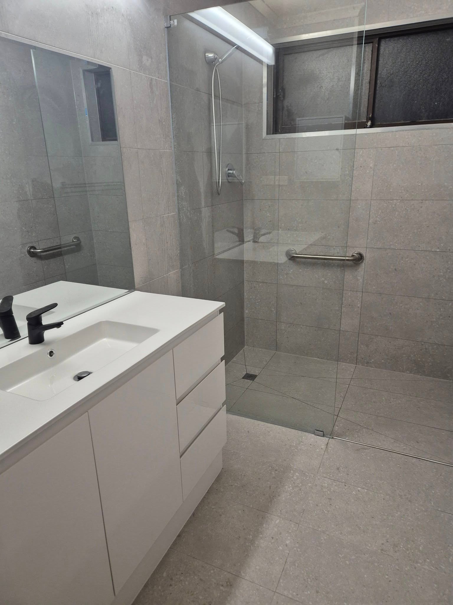 Modern bathroom with white vanity and glass-enclosed shower.