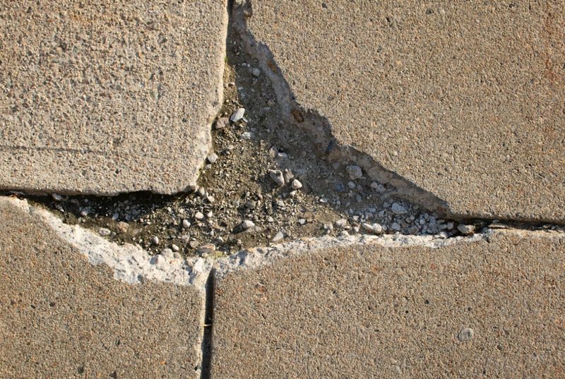 Cracked concrete pavement with exposed gravel underneath.