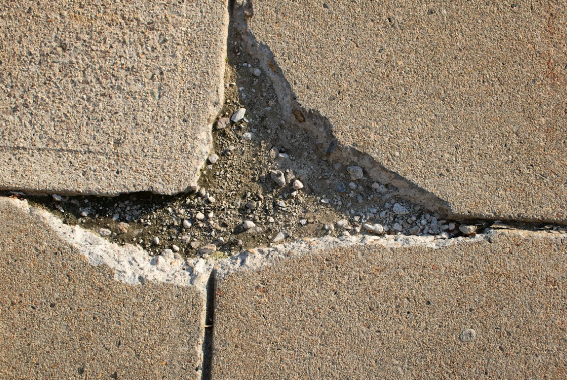 Cracked concrete pavement with exposed gravel underneath.