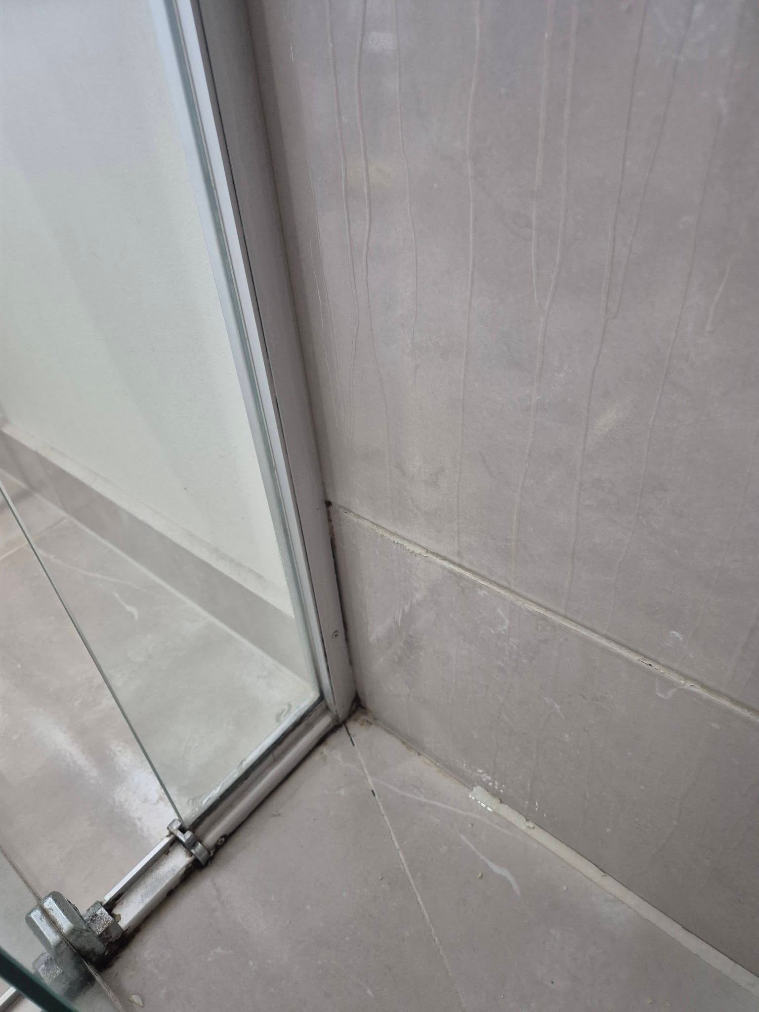 Corner of a glass shower door with tiled wall and floor.